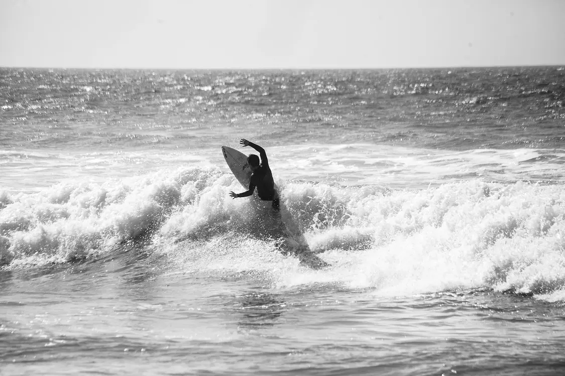 Black-and-white image, zoomed in from a distance, of a surfer turning on a wave